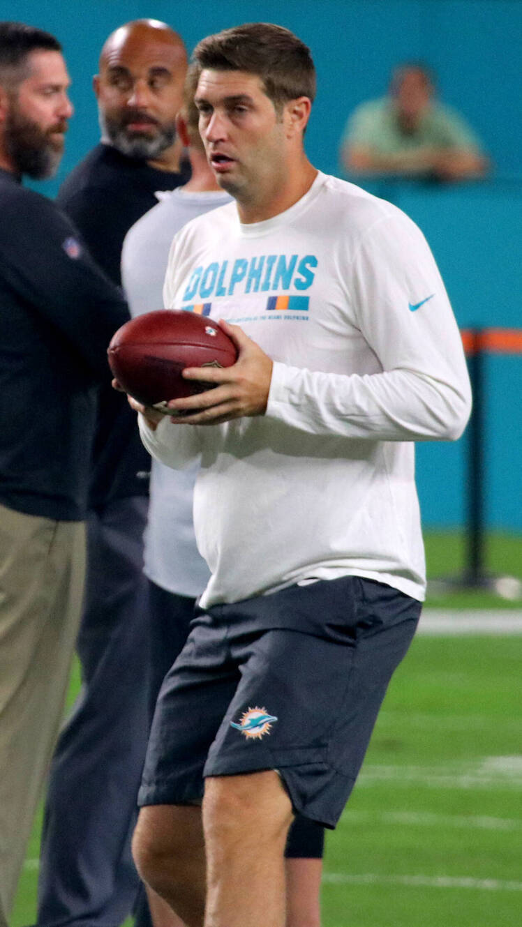 Jay Cutler on the football field during his time with the Miami Dolphins. He is wearing a white long-sleeve team shirt and black shorts with the Dolphins logo, holding a football in both hands as he warms up before a game.